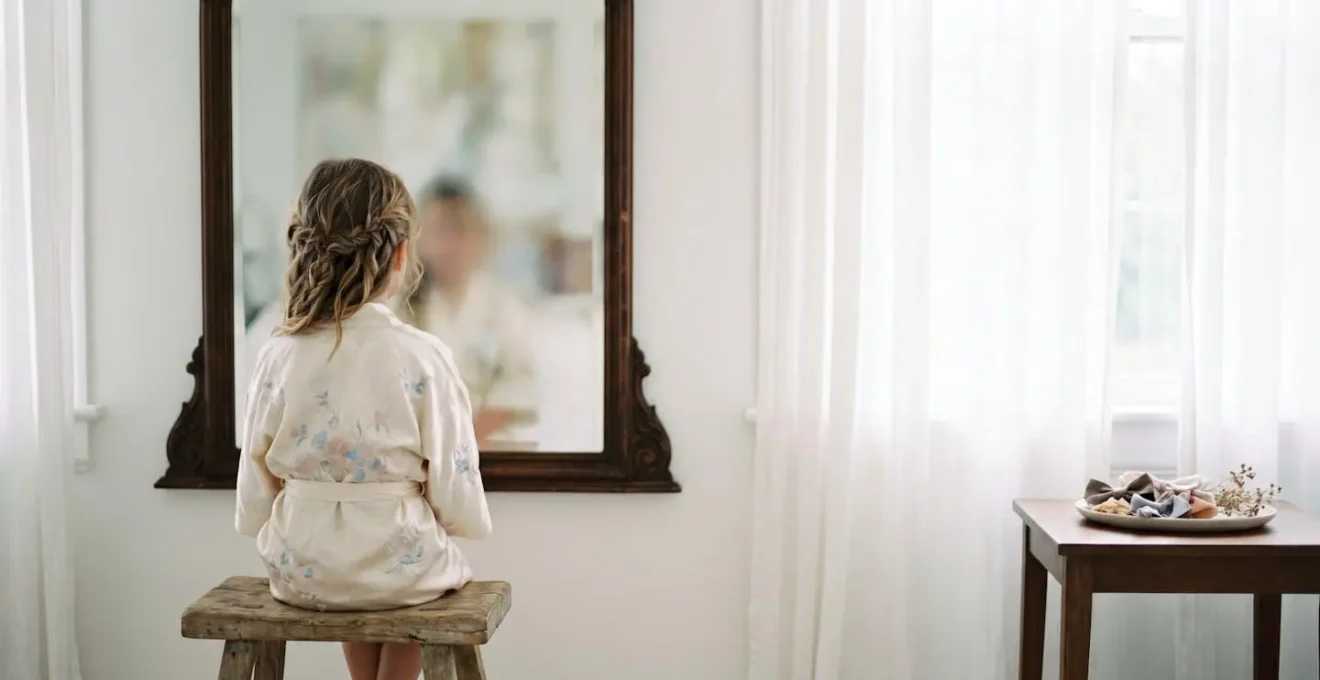 Petite fille souriante assise devant un miroir vintage pendant sa préparation coiffure, ambiance douce et lumineuse