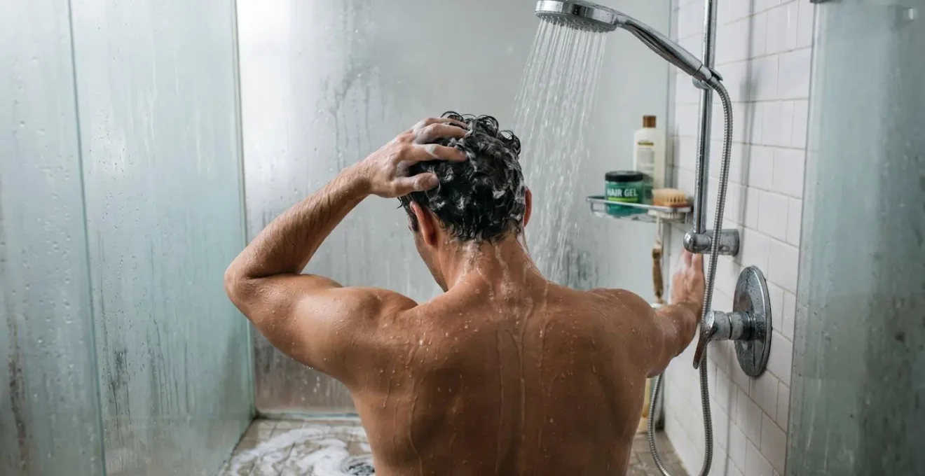 Vue arrière d'un homme rinçant ses cheveux sous la douche pour éliminer le gel