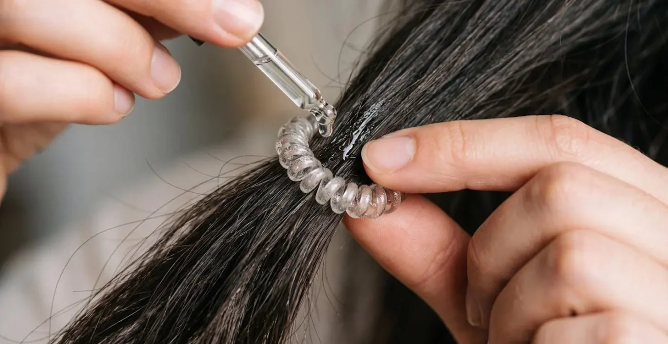 Gros plan sur des mains retirant délicatement un élastique des cheveux avec de l'huile