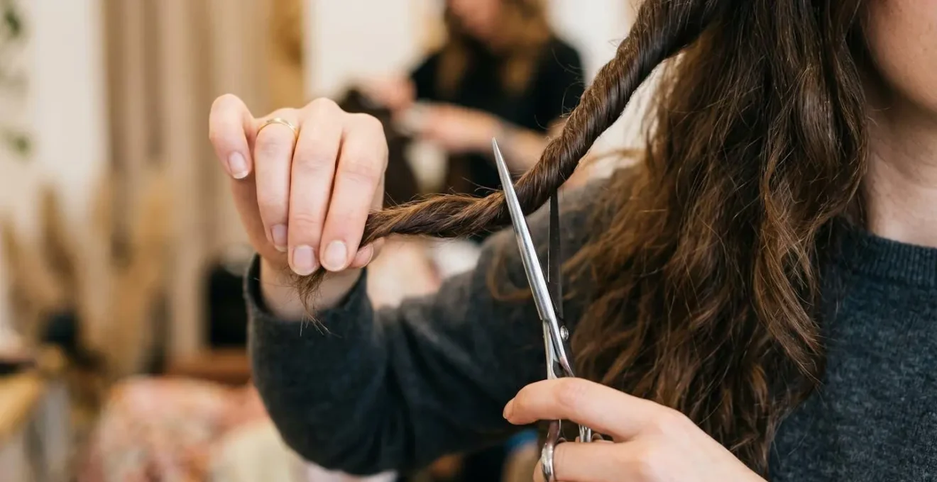 Gros plan sur une main tenant une mèche de cheveux torsadée avec des ciseaux positionnés verticalement