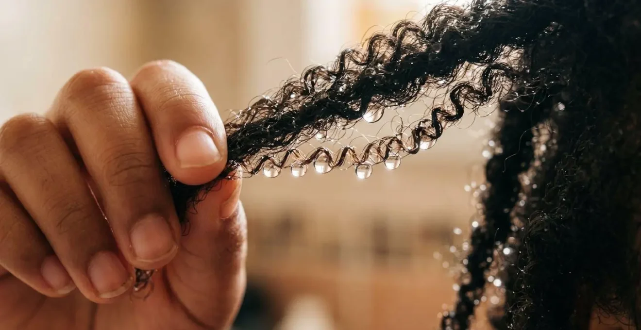 Main d'enfant tenant une mèche de cheveux crépus pendant un test de porosité avec vaporisateur